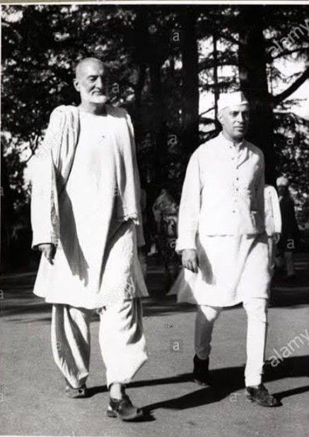 Black and white photograph of Ghaffar Khan walking with Jawaharlal Nehru along a path among pine trees, with a repeated agency watermark across the image.