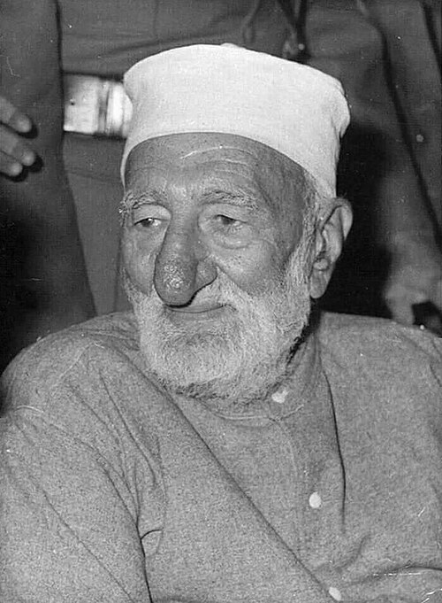 Close portrait of Bacha Khan in old age, wearing a white cap, looking slightly downward.