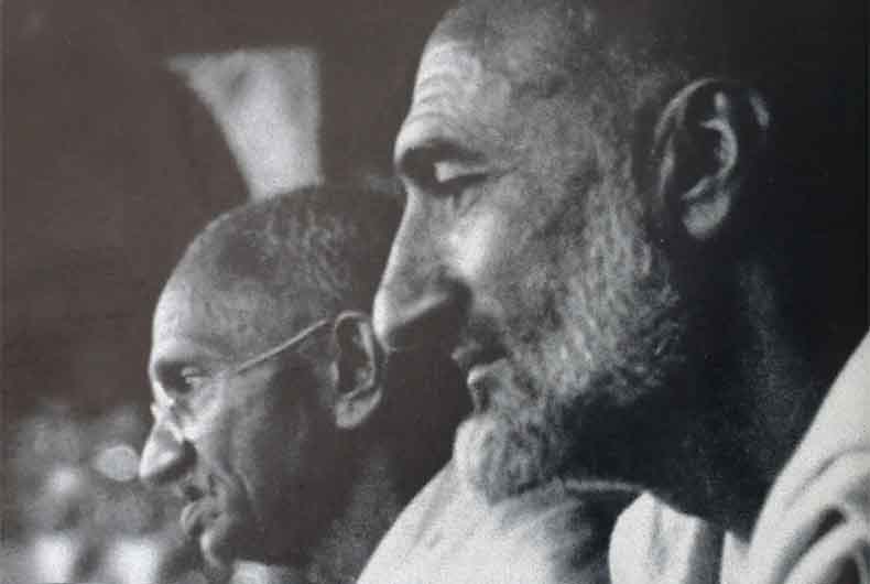 Black and white photograph in profile: Ghaffar Khan in the foreground on the right; Mahatma Gandhi behind him on the left in spectacles, both facing the same direction at a public gathering.